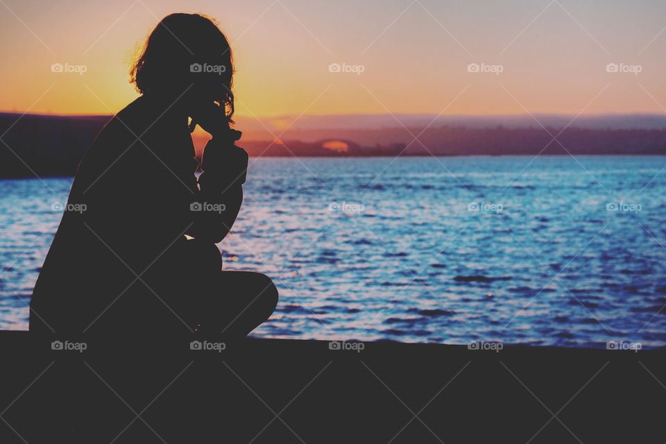 silhouette of a woman by the water during sunset