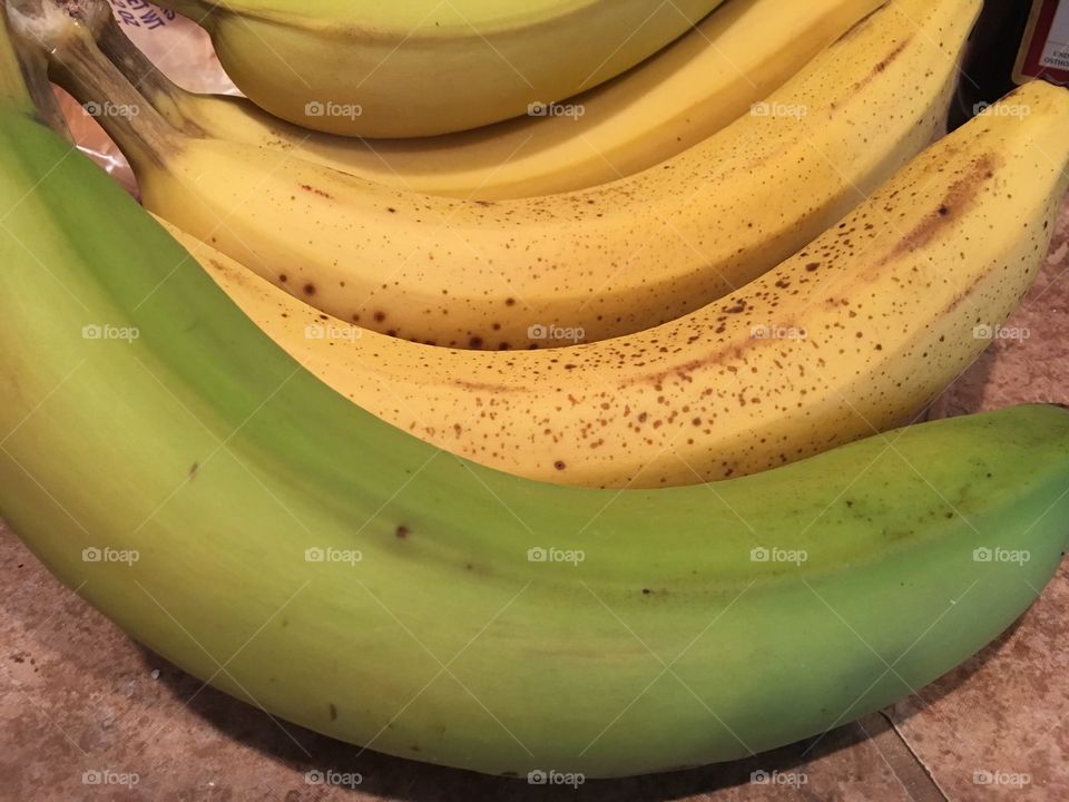 Green banana on a bunch with yellow bananas.