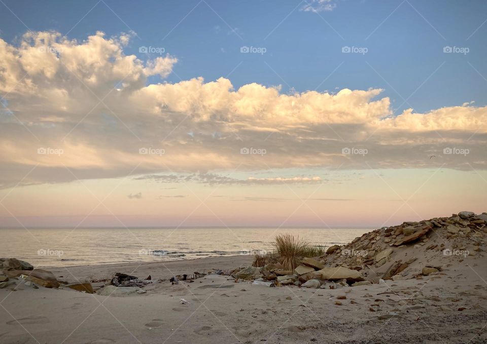 Liquid Fresh water Lake Eerie on Cedar Point shoreline and sandy, rocky beach with purple and blue sunset sky divided by a white puffy cloud 