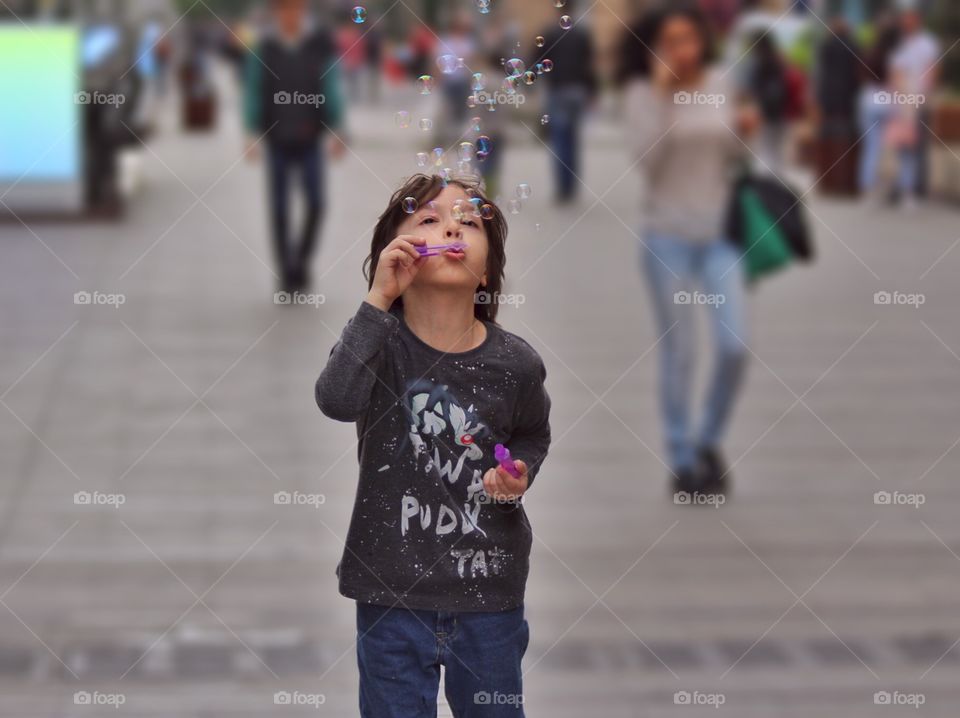 A boy blows soap bubbles on the street