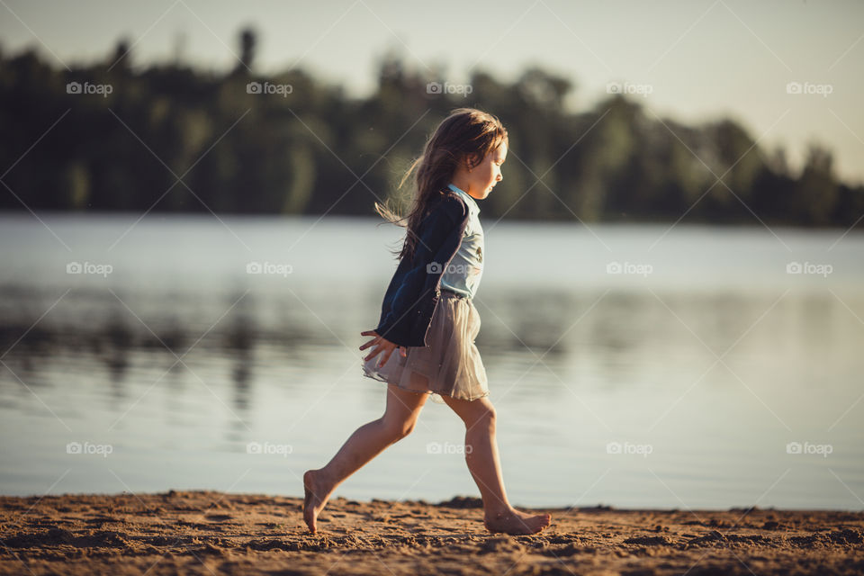 Little girl on lake coast at sunny evening. 