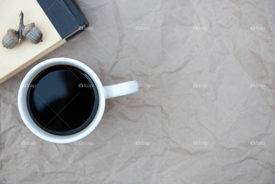 Isolated flat lay of a cup of coffee next to a book on a brown paper background