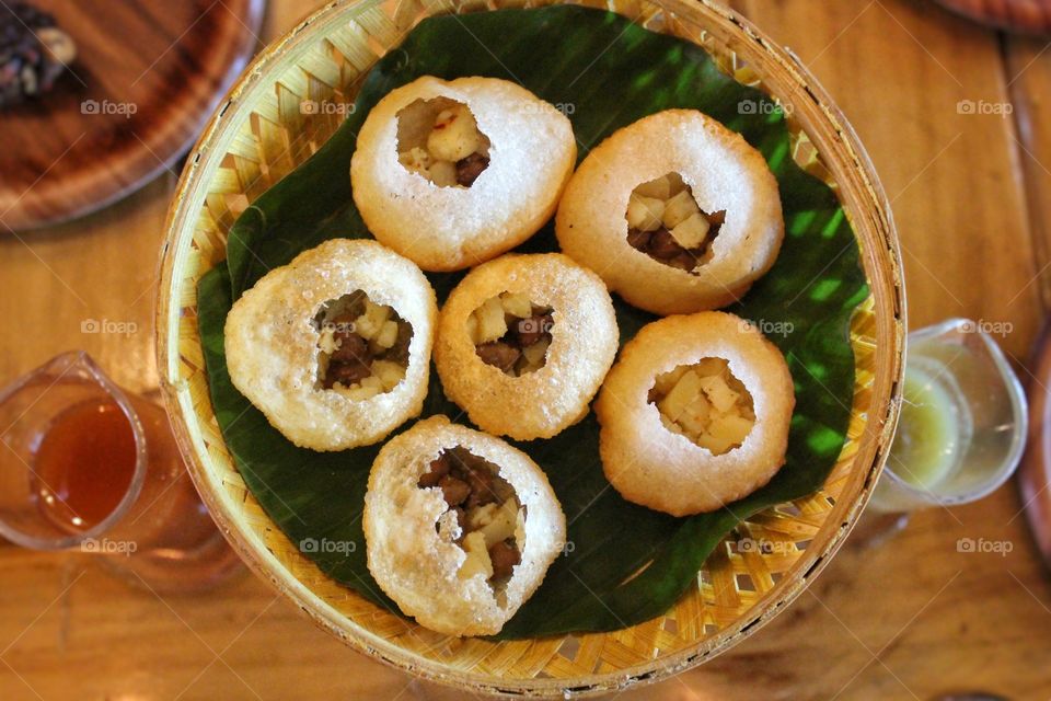 Panipuri is a common street snack in several regions of the Indian subcontinent. It consists of a round, hollow puri, fried crisp and filled with a mixture of flavored water, tamarind chutney, chili, chaat masala, potato, onion or chickpeas