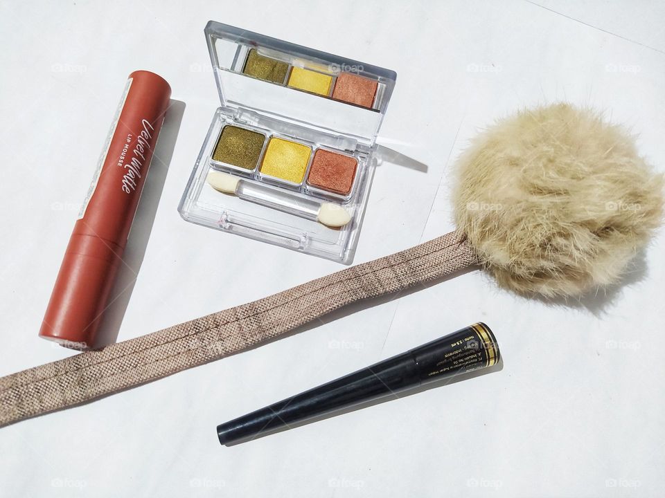 Top view, isolated on white background with lipstick, eyeliner, eyeshadow kit and fluffy ball