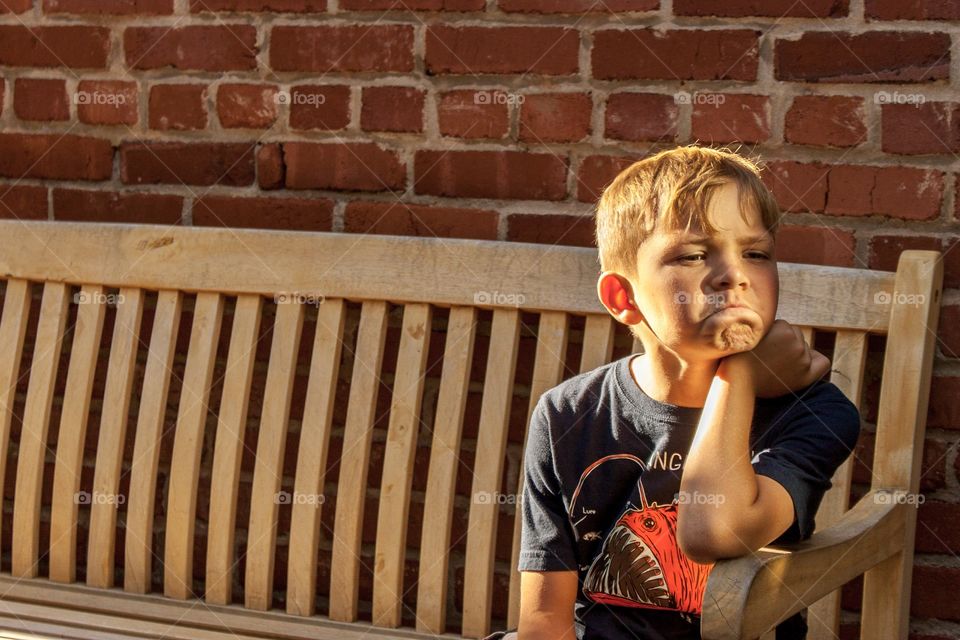 Little boy pretending to sulk on a bench