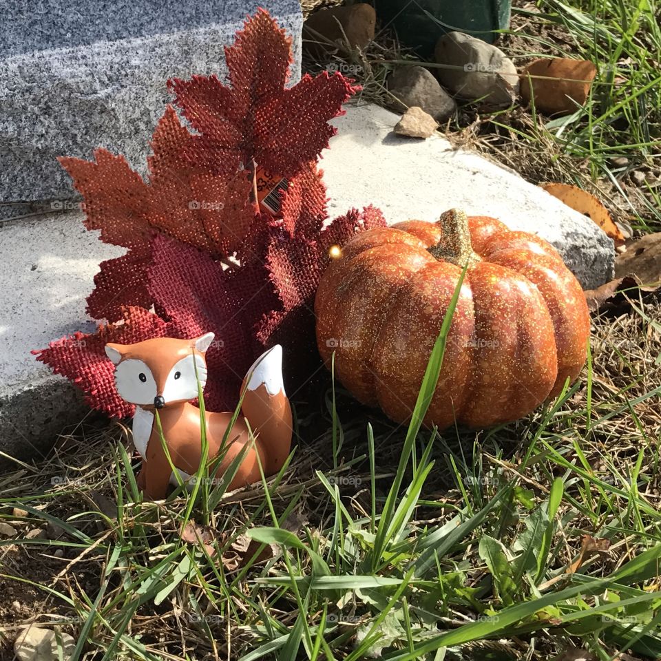 Closeup of a fox figurine and a pumpkin at a gravesite.