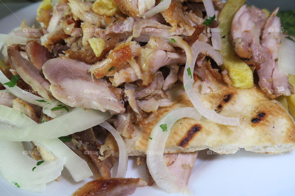 A portion of Greek gyros with chopped chicken meat and pita bread, fried potatoes and onions,  served on a white plate.