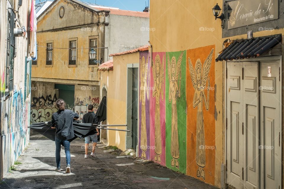 Two men carrying black parasols in a narrow alley in Alfama, Lisbon, Portugal