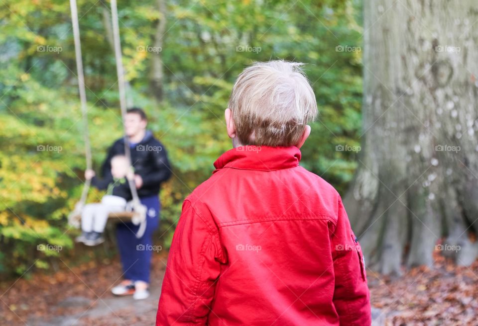 Kid watching other kid on a swing with parent 