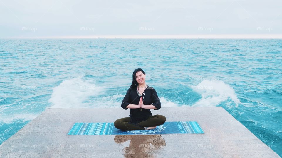 Woman in sports clothing practicing yoga and meditation on pier seaside in bad rainy weather 