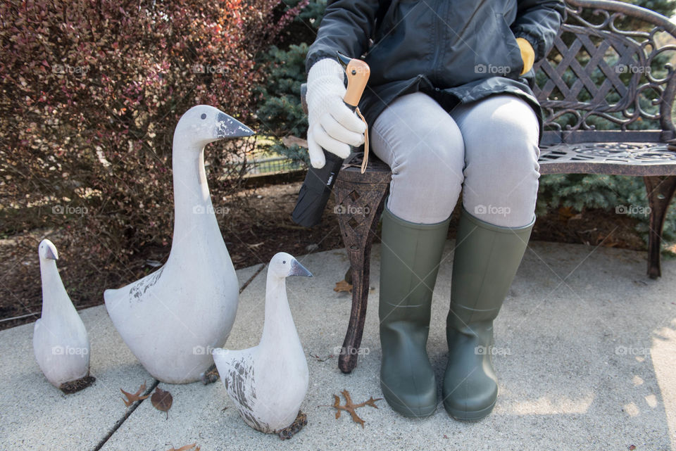 Young woman sitting on a bench outdoors next to decorative ducks