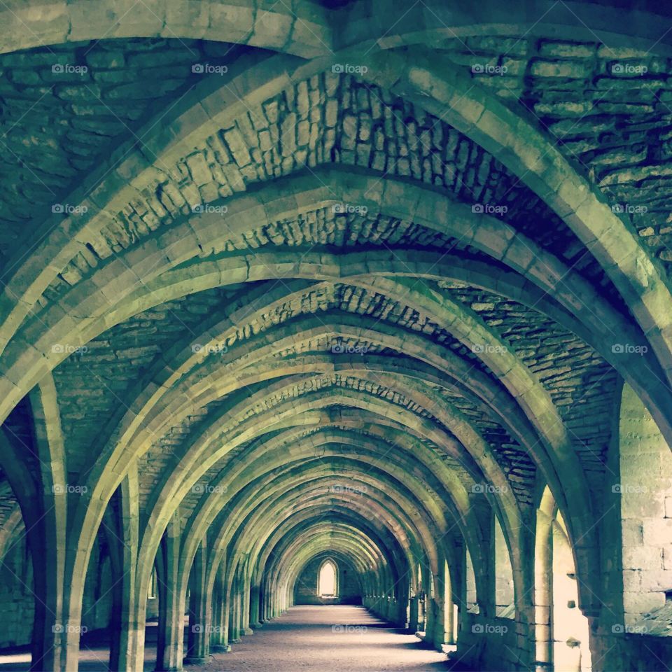 Underground cellar at abbey with curved, vaulted, stone ceiling and light at the end of the tunnel 