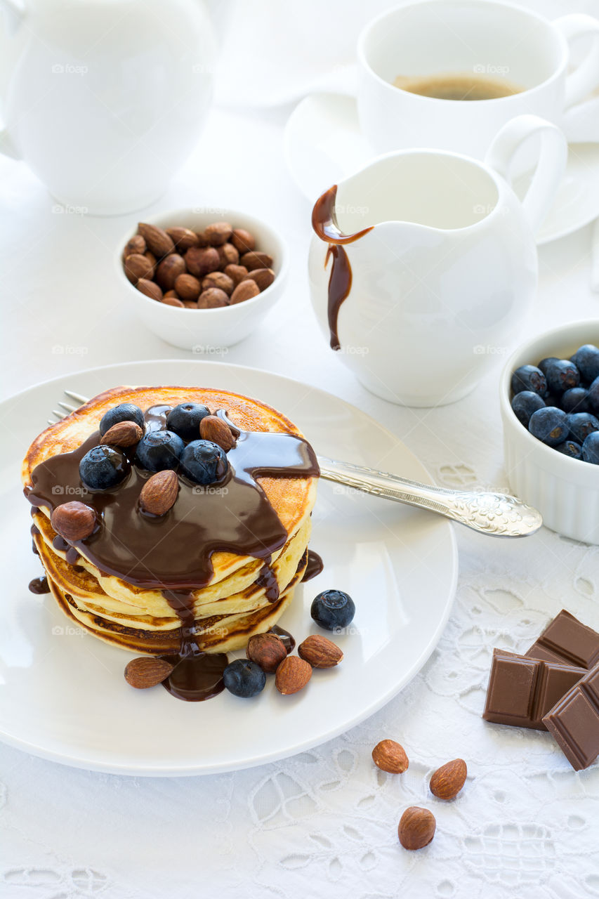Stack of pancakes with chocolate sauce, blueberries and nuts