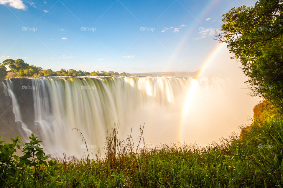 Sunset over Vic falls waterfall in Africa with two rainbows grass and blue skies.