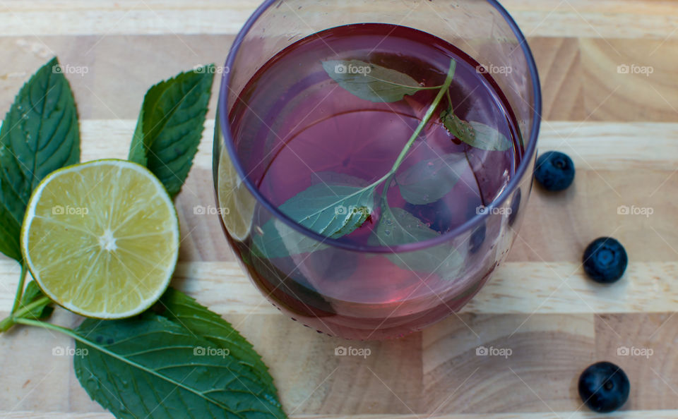 Homemade antioxidant rich hydrating Blueberry Lime cocktail juice with mint refreshing summer twist on berry lemonade - blueberry limeaid high angle view on wood table with fresh mint leaves and lime 