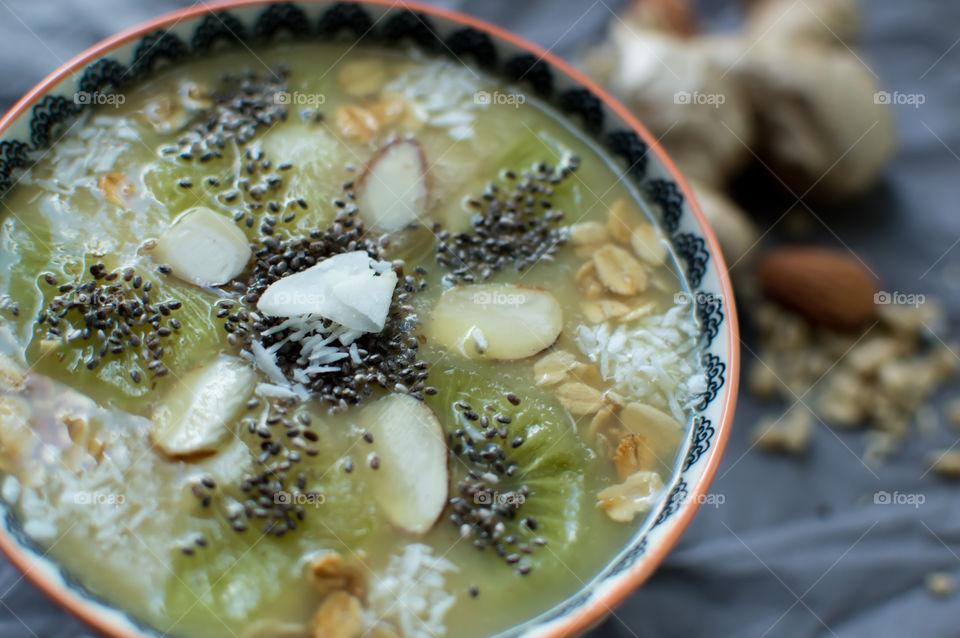 Closeup green fruit smoothie bowl with mandala design made of fresh healthy superfoods smoothie ingredients including kiwi, coconut, chia seed, nuts and granola in mandala design garnish