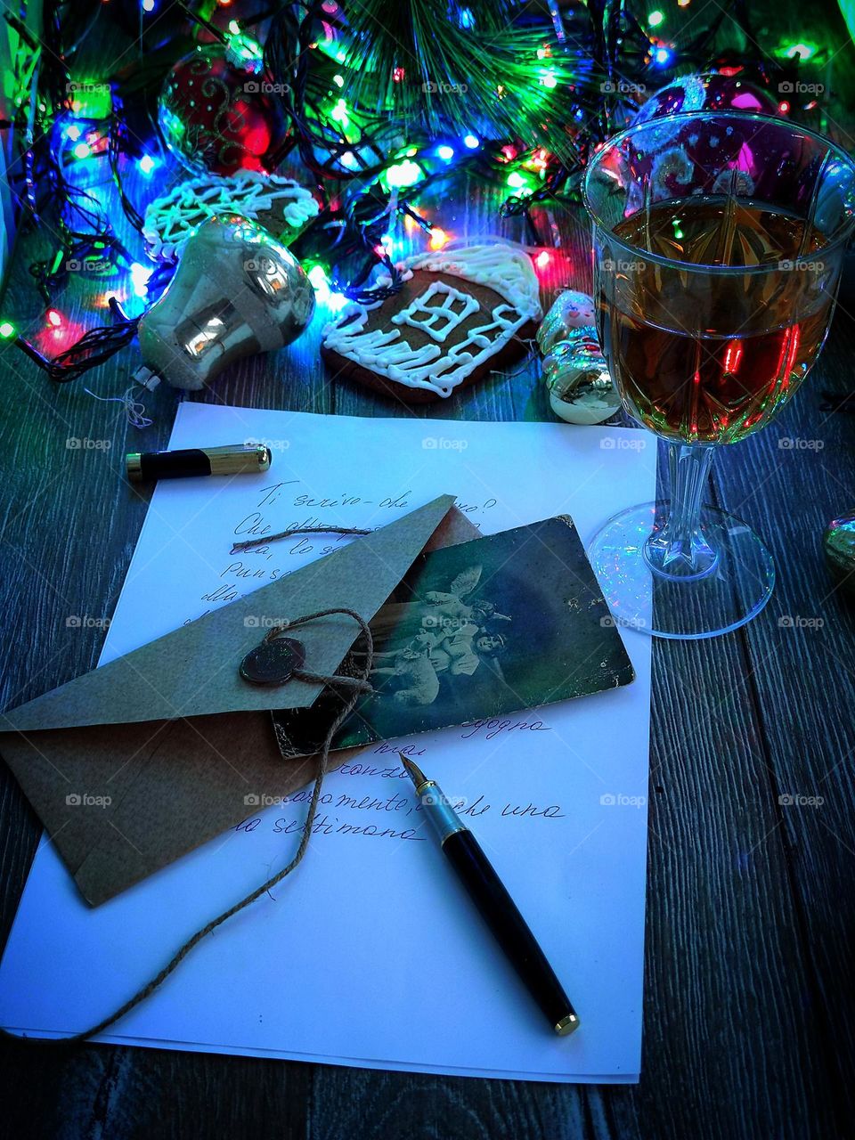 Write letters to loved ones and family that keep their warm. A sheet of paper with handwritten text, a fountain pen, an envelope, an old photograph with a Christmas greeting.There is a glass of wine nearby, Christmas decorations, a gingerbread house