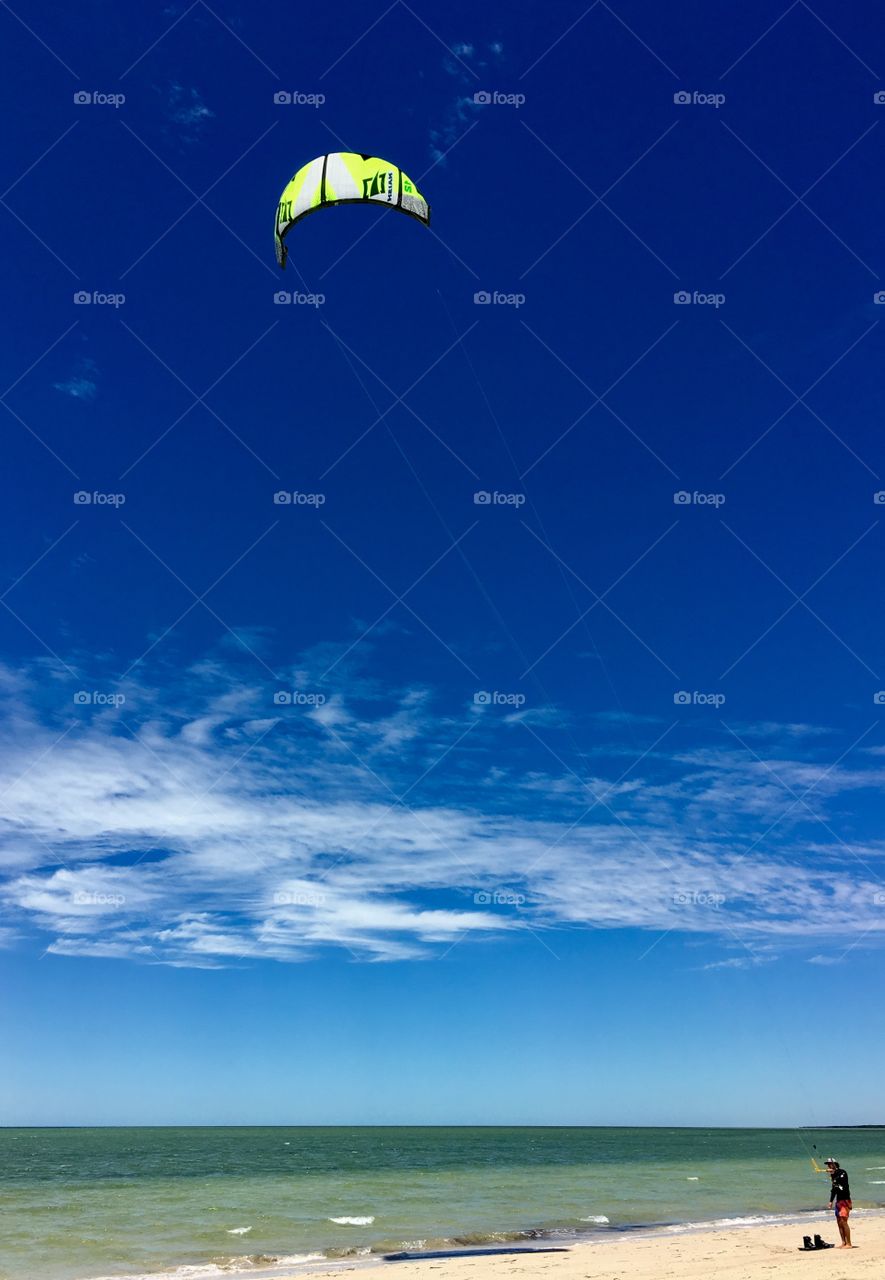 Kiteboarding, colourful kite board kite in vivid blue wispy sky at ocean shore