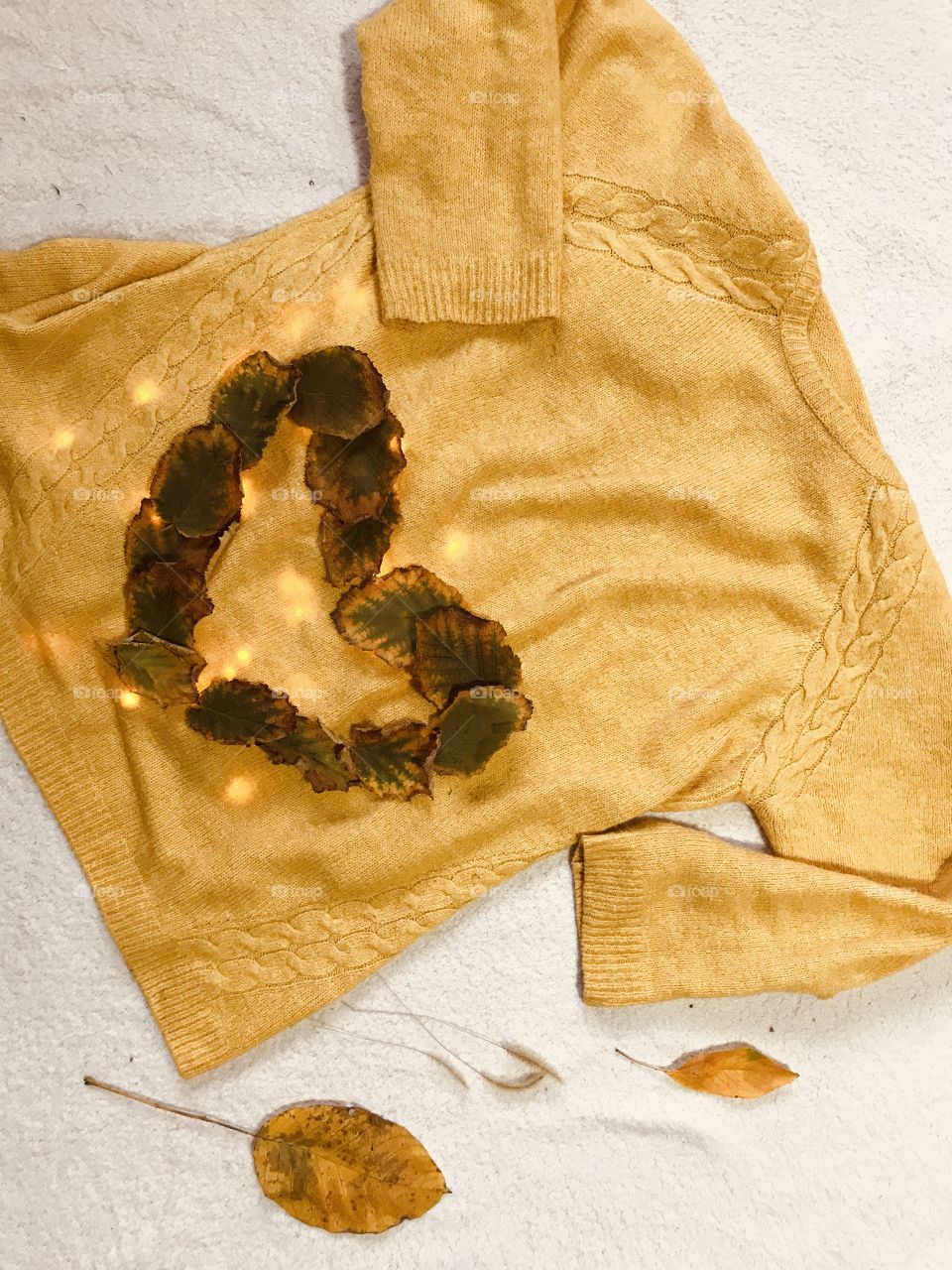 Yellow sweater with autumn leaves in a shape of a heart.