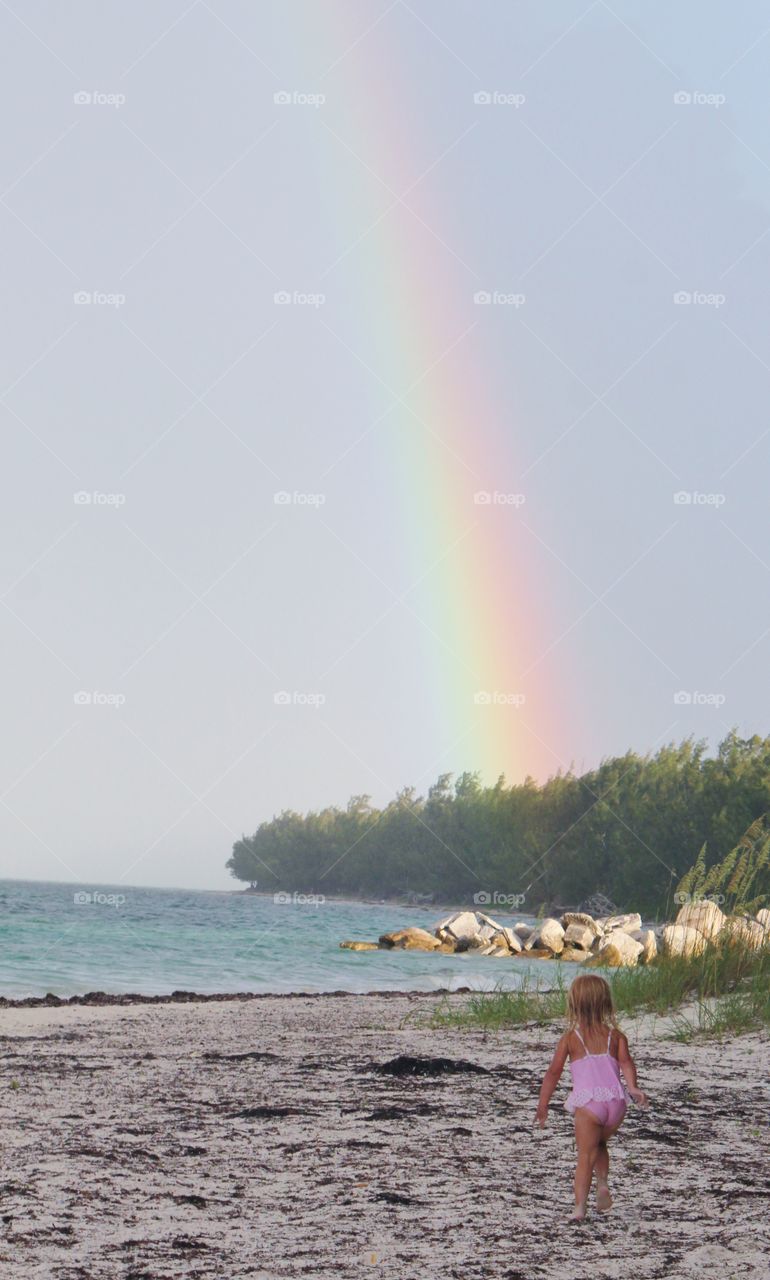 Little girl chasing a rainbow at the beach