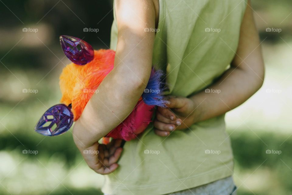 Unrecognisable child wearing green shirt holding cute fluffy toy in hands