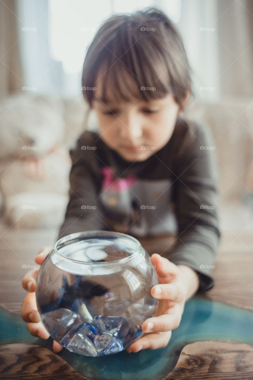 Little girl with fish in round aquarium at home