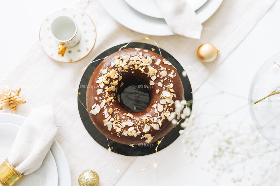 Large round chocolate almond cake on the table with New Year serving, christmas white scandinavian festive table, top view, winter flat lay