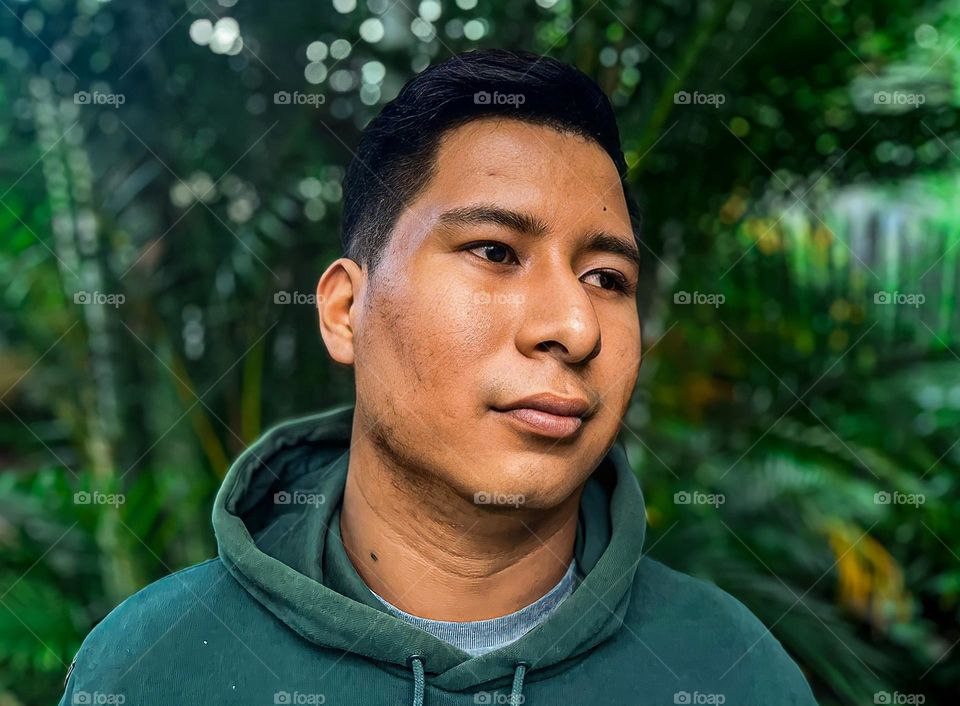 dark-skinned man in profile, with pimples and pimple scars, with vegetation background