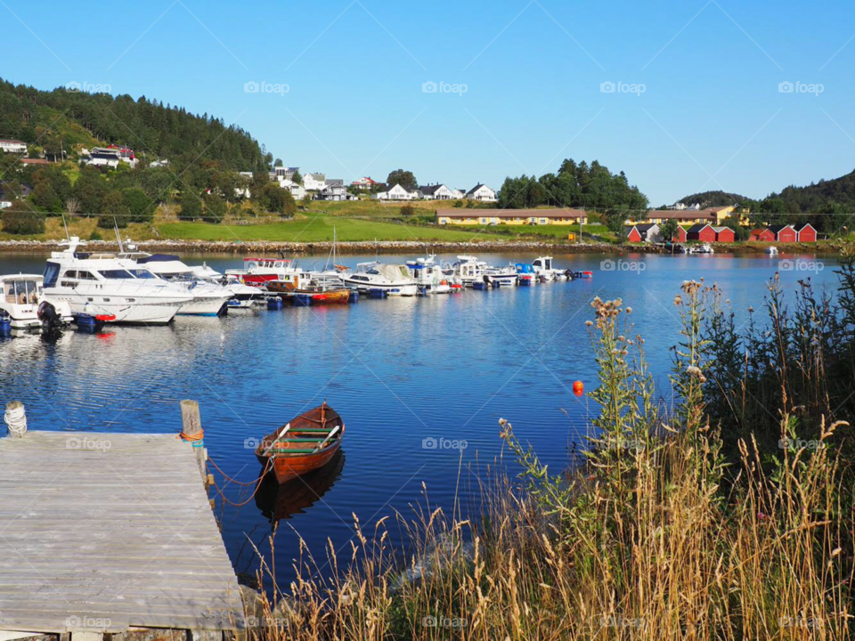 Red wooden boat attached to jetty on pretty coastal town in Norway.