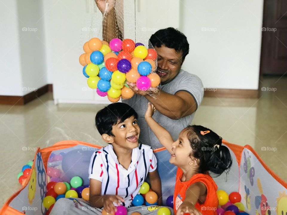 Father poring balls on kids in ball pit, and kids enjoying with father a lot