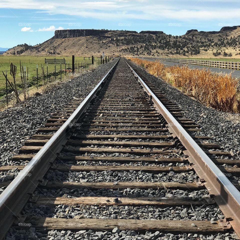 Symmetrical train tracks run up to the foot of a butte in rural Crook County in Central Oregon on a sunny day. 