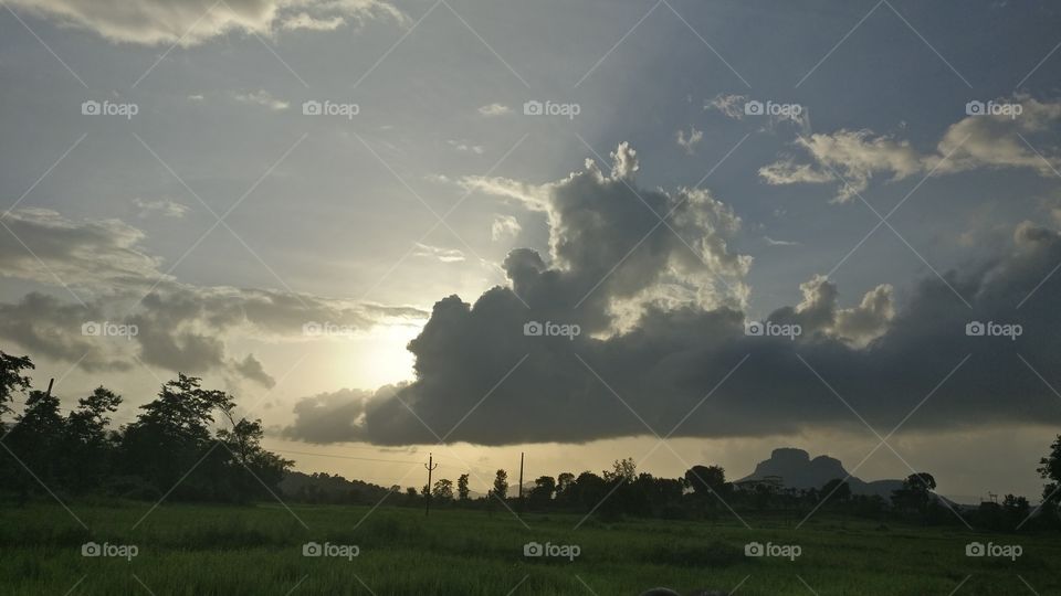CLOUDY ATMOSPHERE, Sun behind clouds, sunrays trying to reach to us through sidelines. Mix of black, gray and white cloud shades. A beautiful atmosphere, lush green grass and a beautiful, lovely evening!