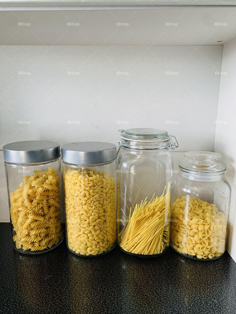 Different pasta types of pasta shapes in glass storage containers. Fusili, elbows spaghetti and shells aligned in a line in the kitchen