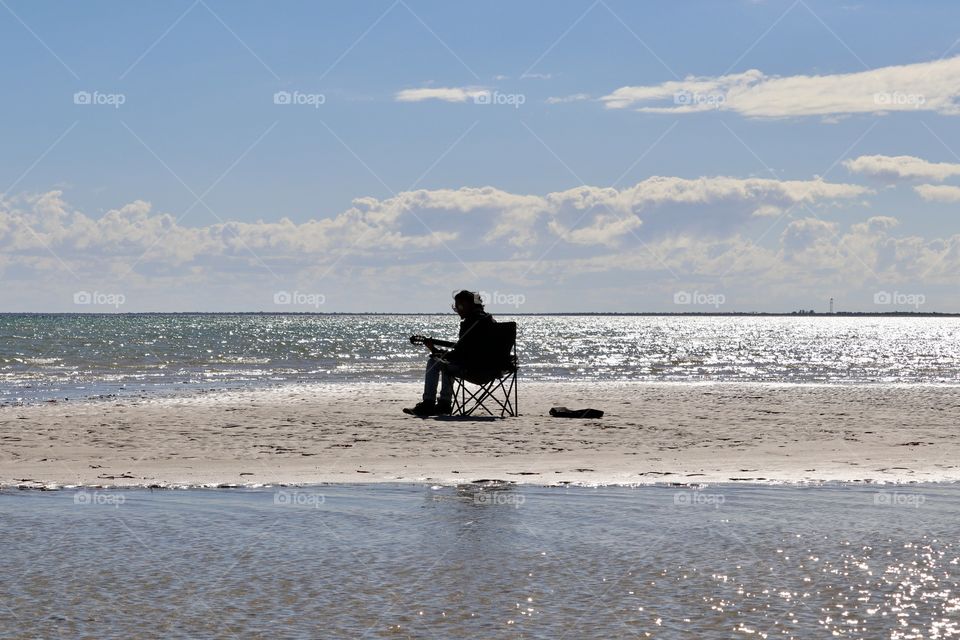 Silhouette of male musician playing guitar and singing surrounded by glistening ocean late day golden hour