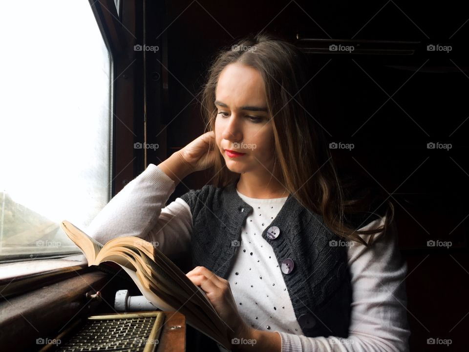 Woman wearing autumn clothes reading in train near the window