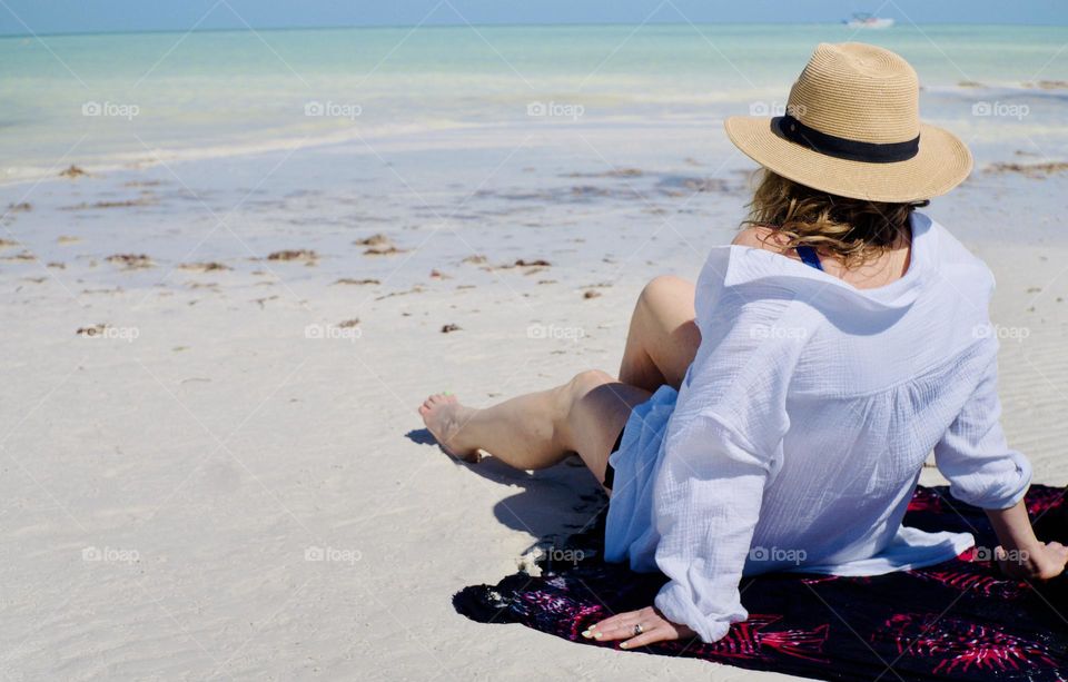 A beautiful woman sits on a sarong admiring the amazing colours of the sea.