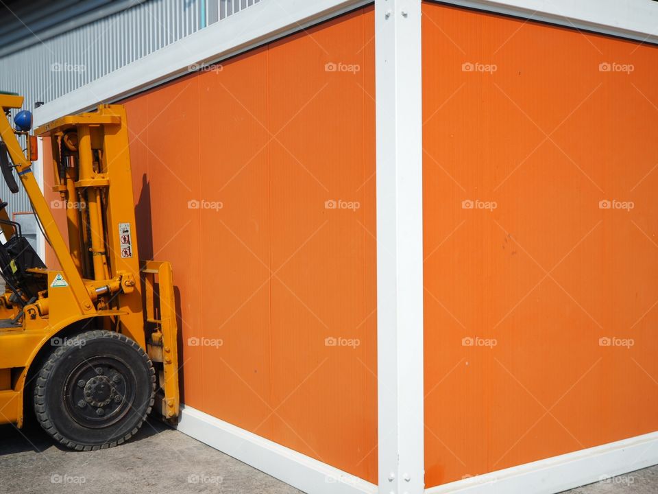 A forklift vehicle is in position for lifting the orange color container.