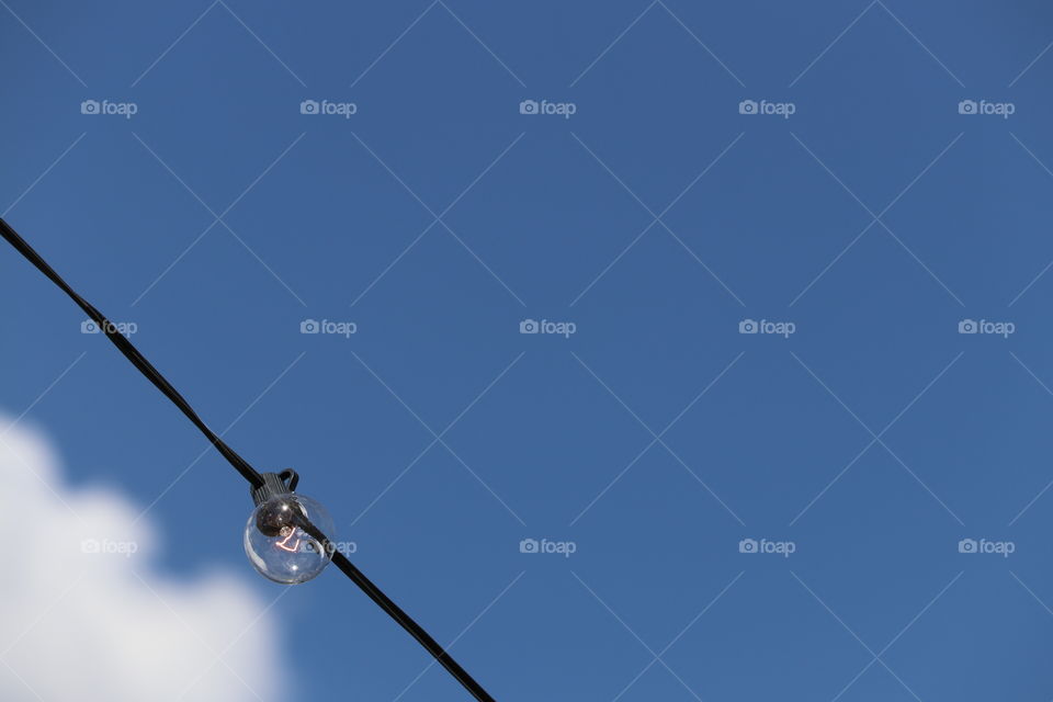 Clear glass round light bulb lighted on an electrical wire against vivid clear blue sky, minimalistic with plenty of room for text 