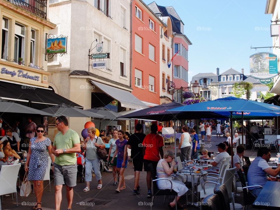 Crowds of people out walking, shopping, and eating, on Luxembourg streets on a summer day. 