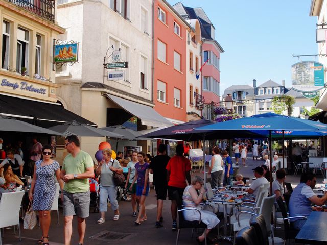 Crowds of people out walking, shopping, and eating, on Luxembourg streets on a summer day. 