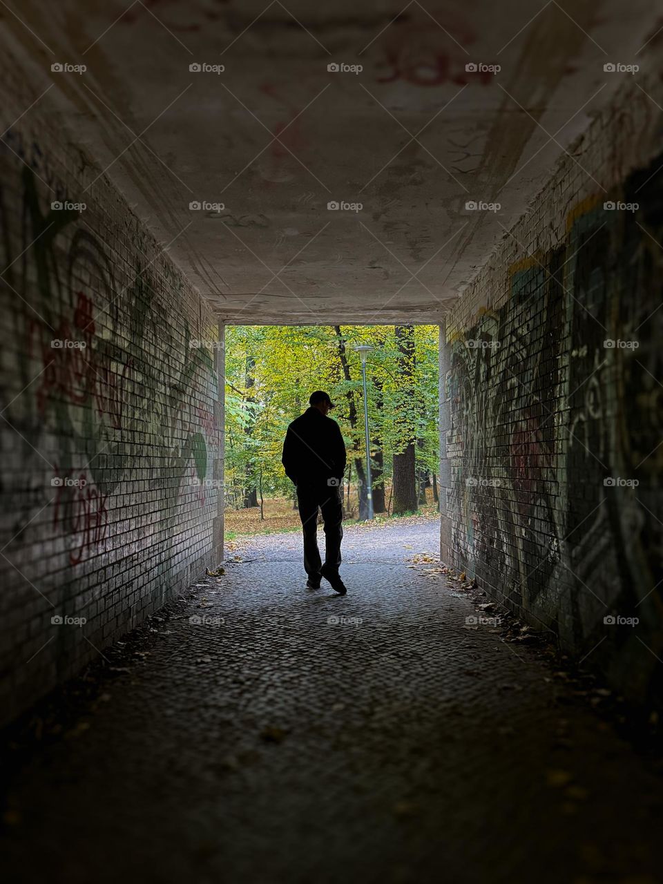 Dark silhouette of a man in the tunnel with graffiti, going from the darkness to the light 