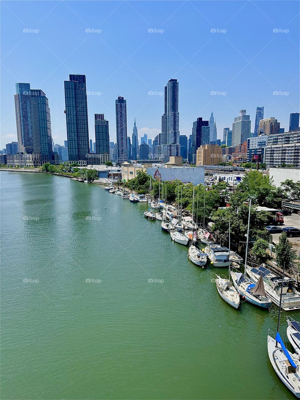 This is “Newtown Creek”, an ocean inlet of the “East River” with many picturesque boats seen from the “Pulaski Bridge” that connects “Greenpoint”, Bklyn to LIC, Queens in the bright afternoon summertime sunshine. 2024. Hypnotic Productions