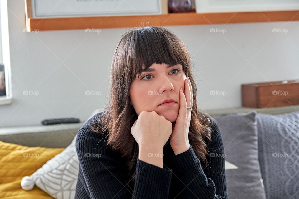 Sad and worried girl sitting on sofa at home