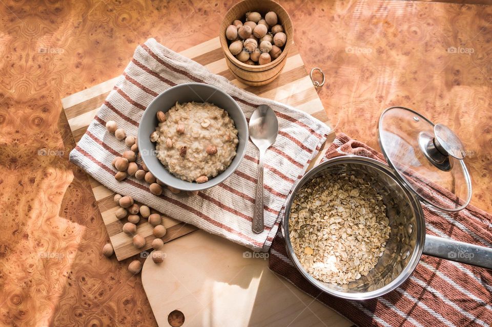 Cooked oatmeal in a deep gray plate with hazelnuts and honey.