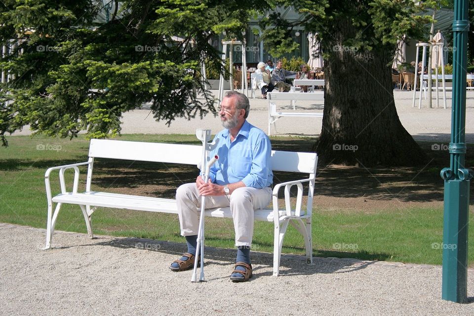 Man with a crutch sitting on the bench in the park 