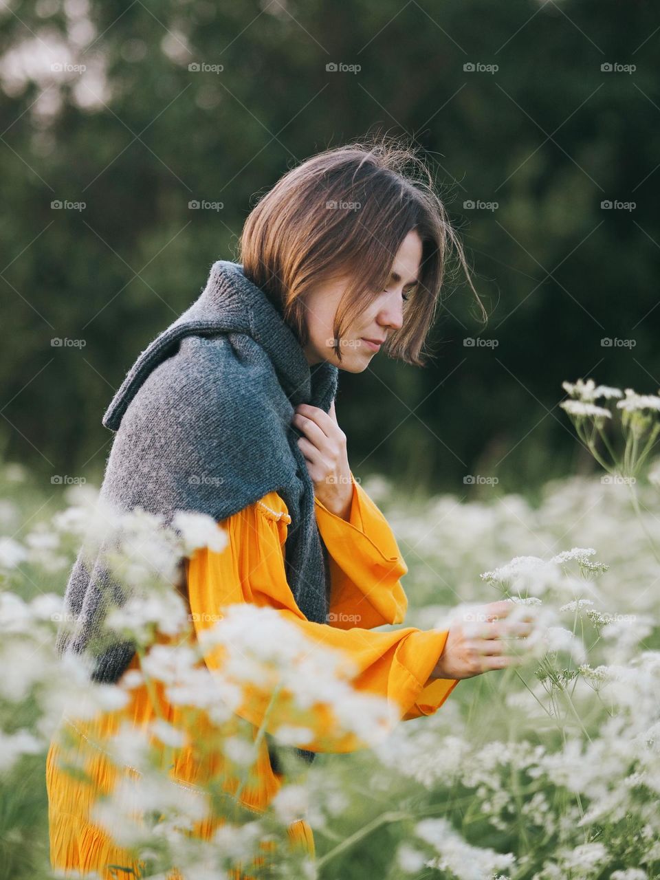 Young beautiful brunette woman wearing yellow dress walking in blooming field in summer day, portrait of woman 