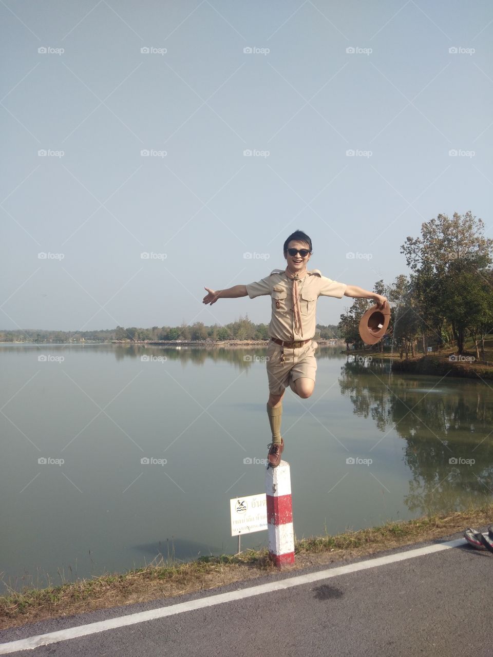 A Man wear scout suits, standing balance with one leg on top of concrete pillars along the reservoir