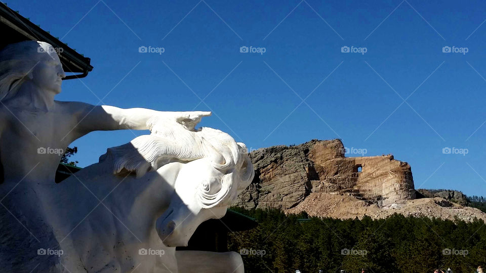 The Crazy Horse statue with the actual monument behind it on a beautiful blue sky day.