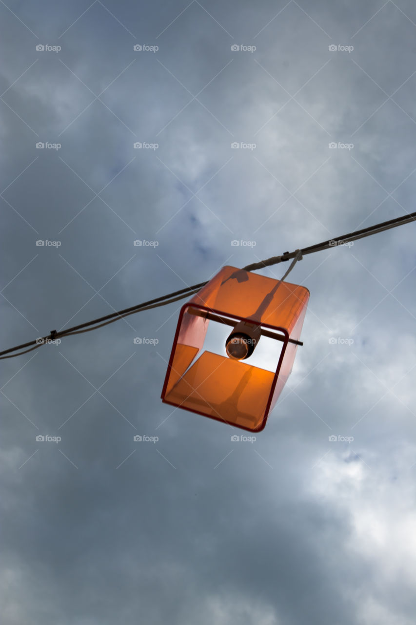 an orange glas lamp hanging outside against a dark rainy sky