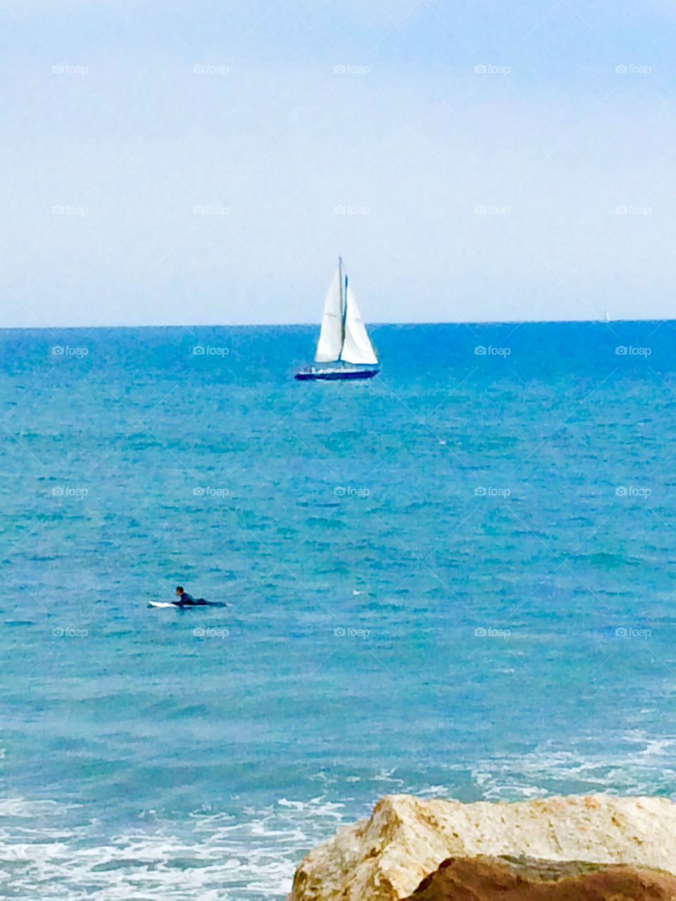Going my way?. Surfer swimming out by a sailboat at Will Rodgers Beach